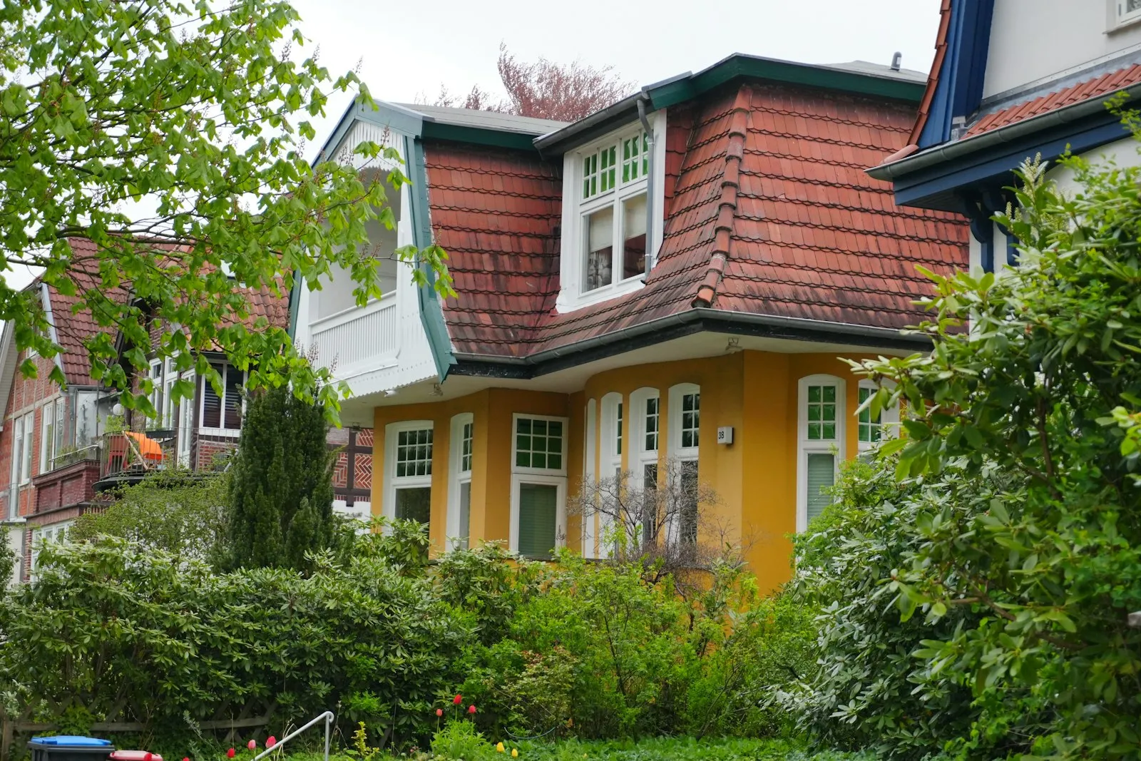Casa amarela com telhado vermelho e jardim na frente