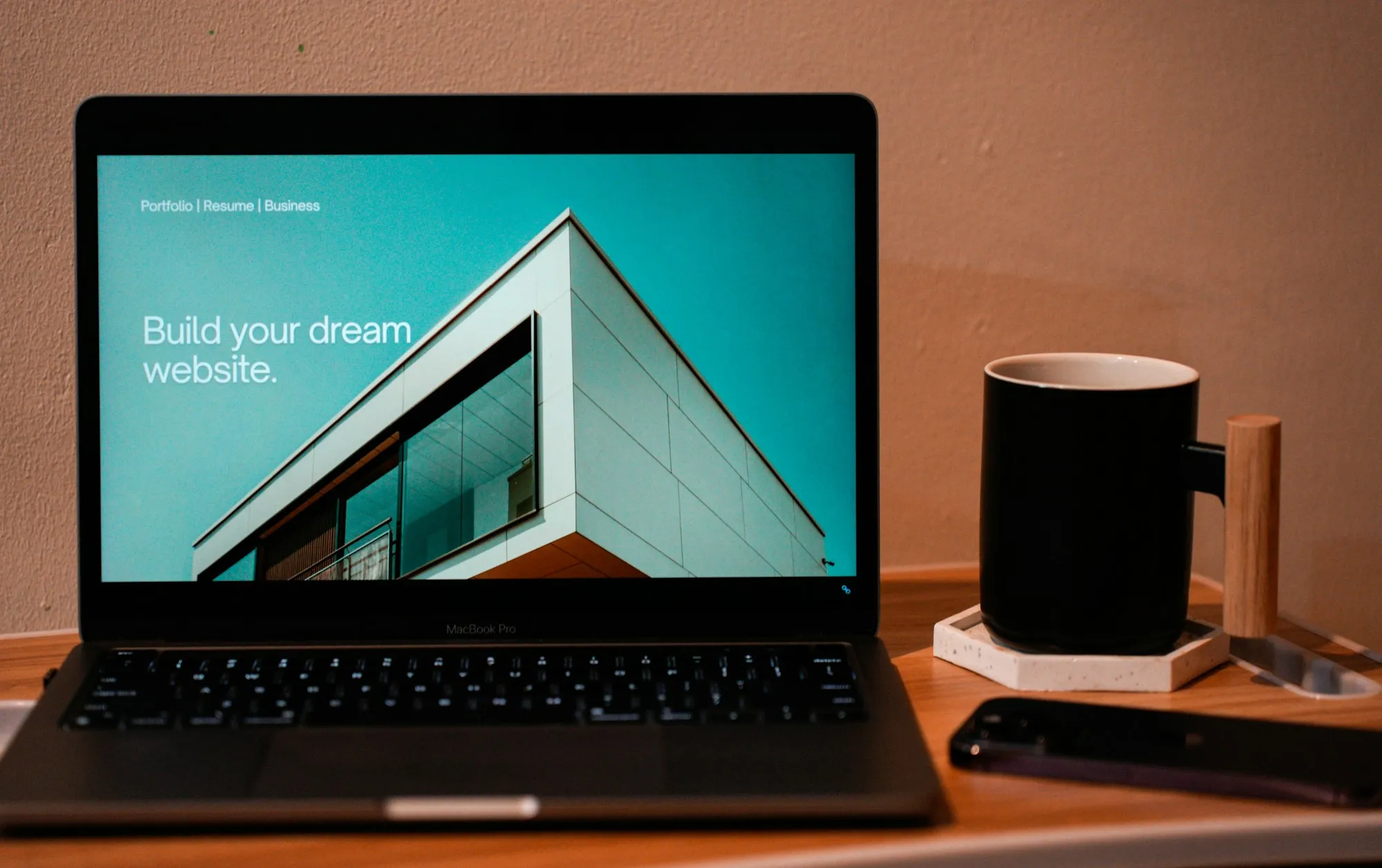 Notebook sobre mesa de madeira mostrando a página inicial de um site com a frase build your dream website