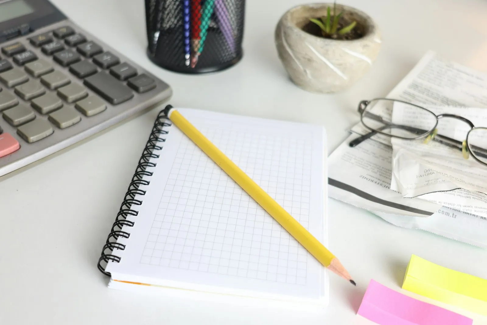 Calculadora, caderno quadriculado e óculos sobre uma mesa com papéis