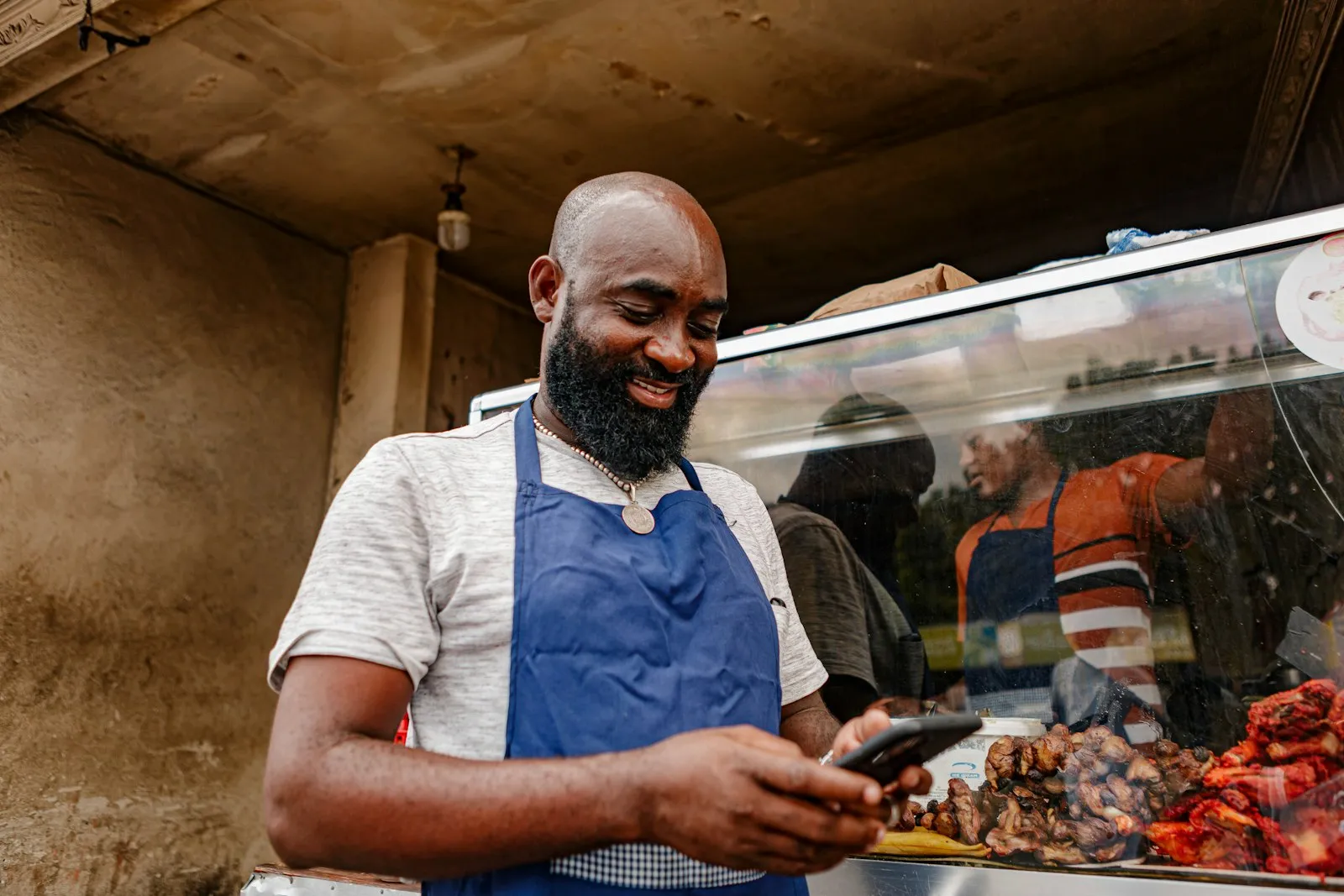 Comerciante sorrindo enquanto usa o celular atrás do balcão da loja