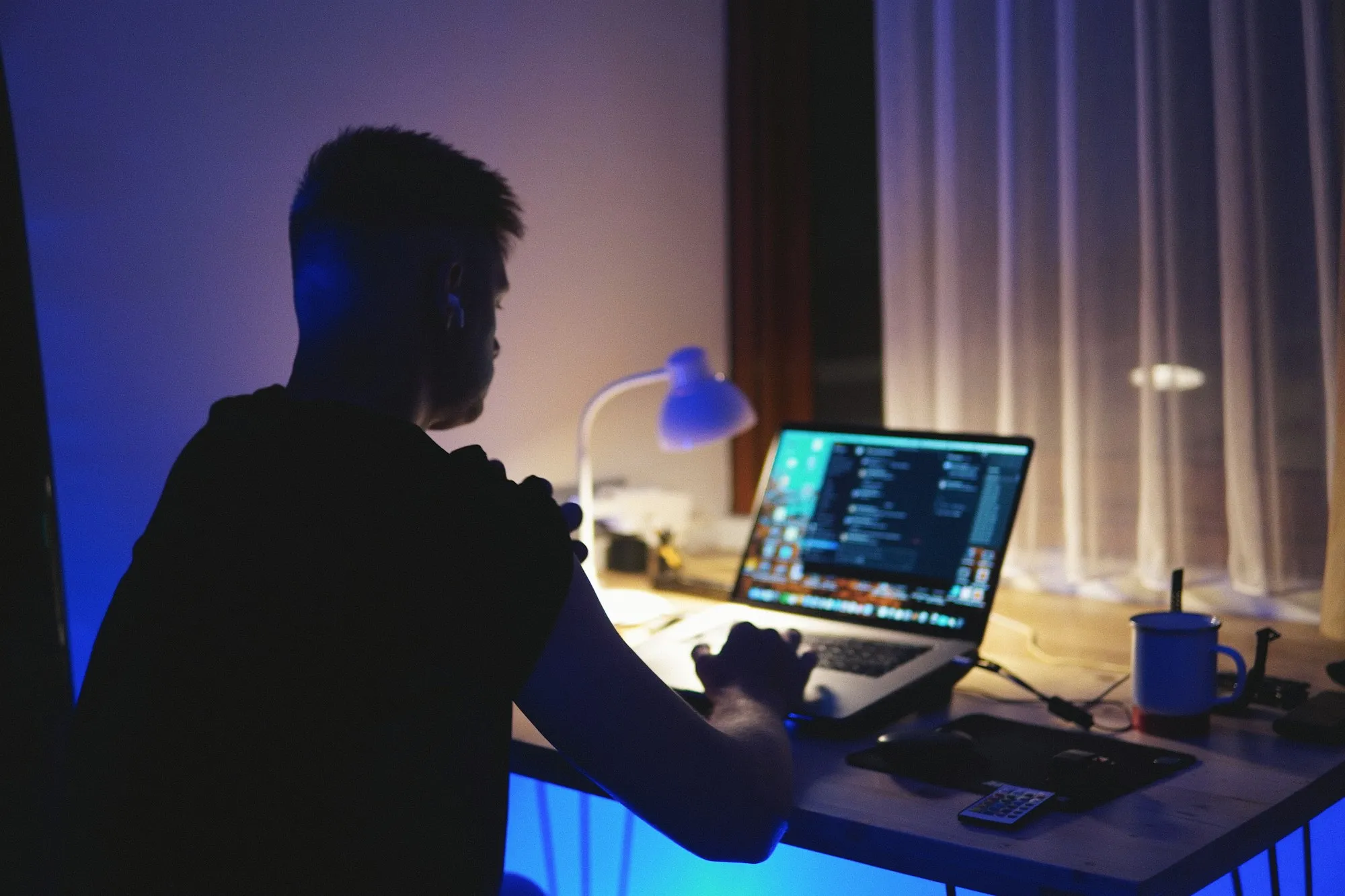 Desenvolvedor programando à noite em notebook iluminado por luminária azul